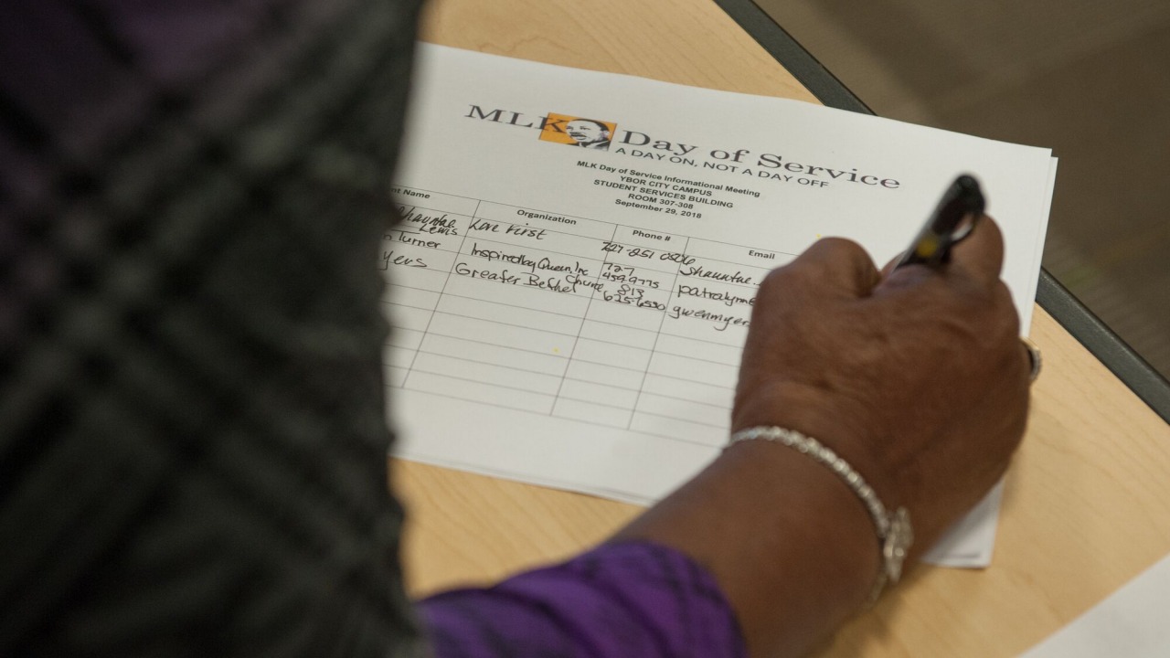 Person's hand filling out a sign-in sheet for MLK Day of Service informational meeting