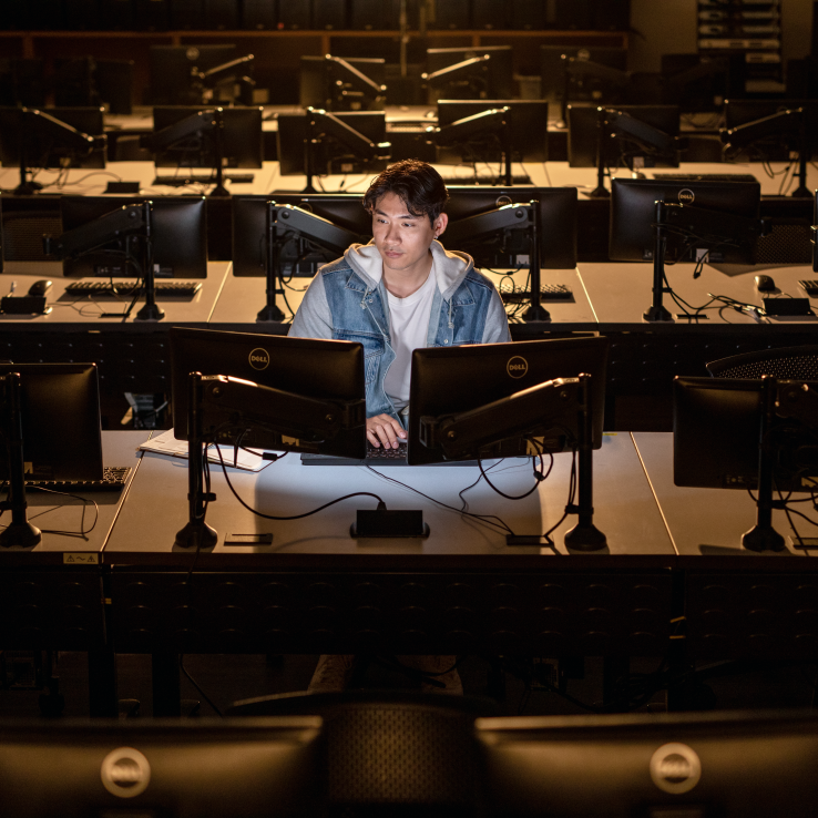Male student working on a computer screen in an empty classroom.