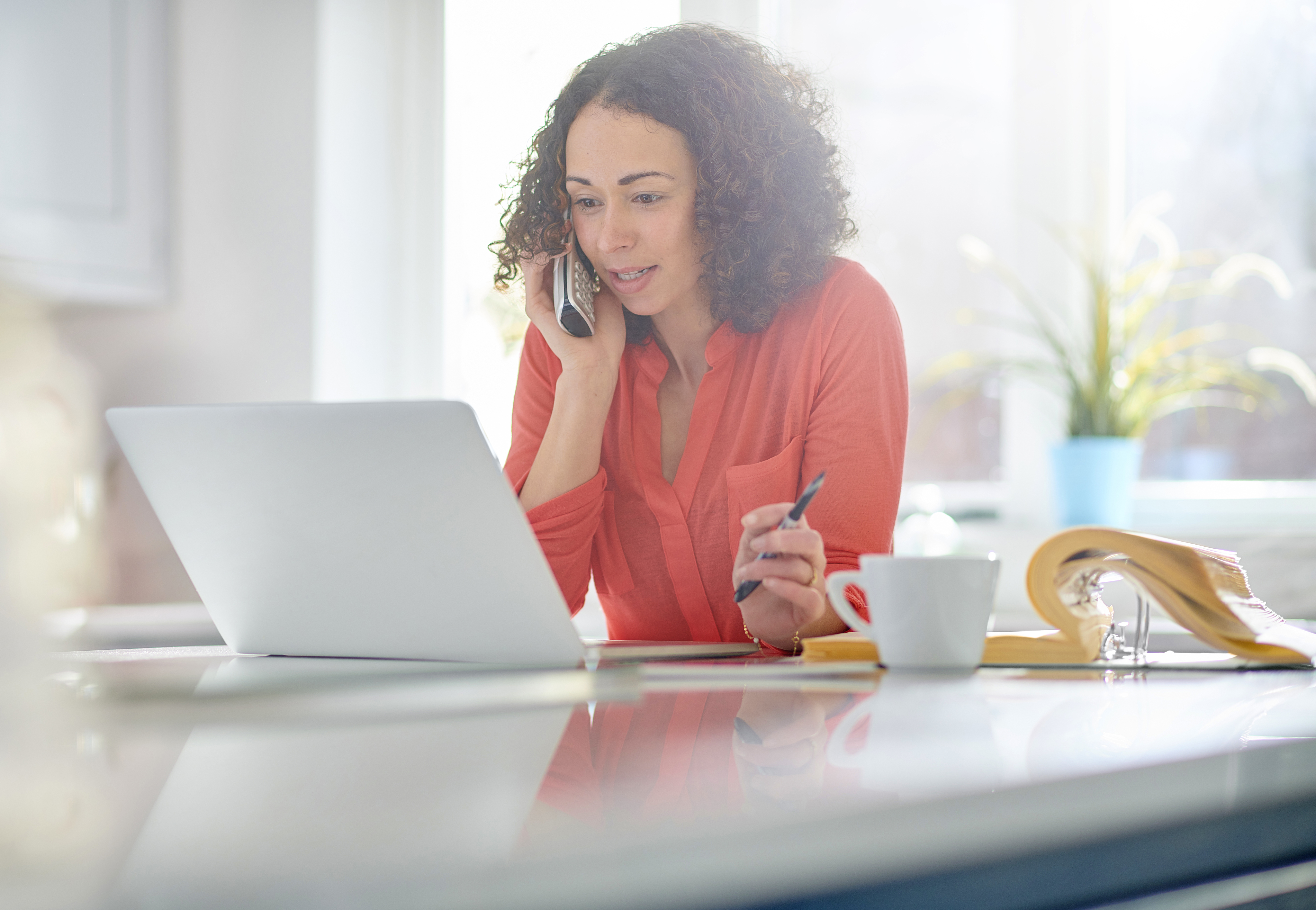 a woman  in her kitchen paying a bill by phone