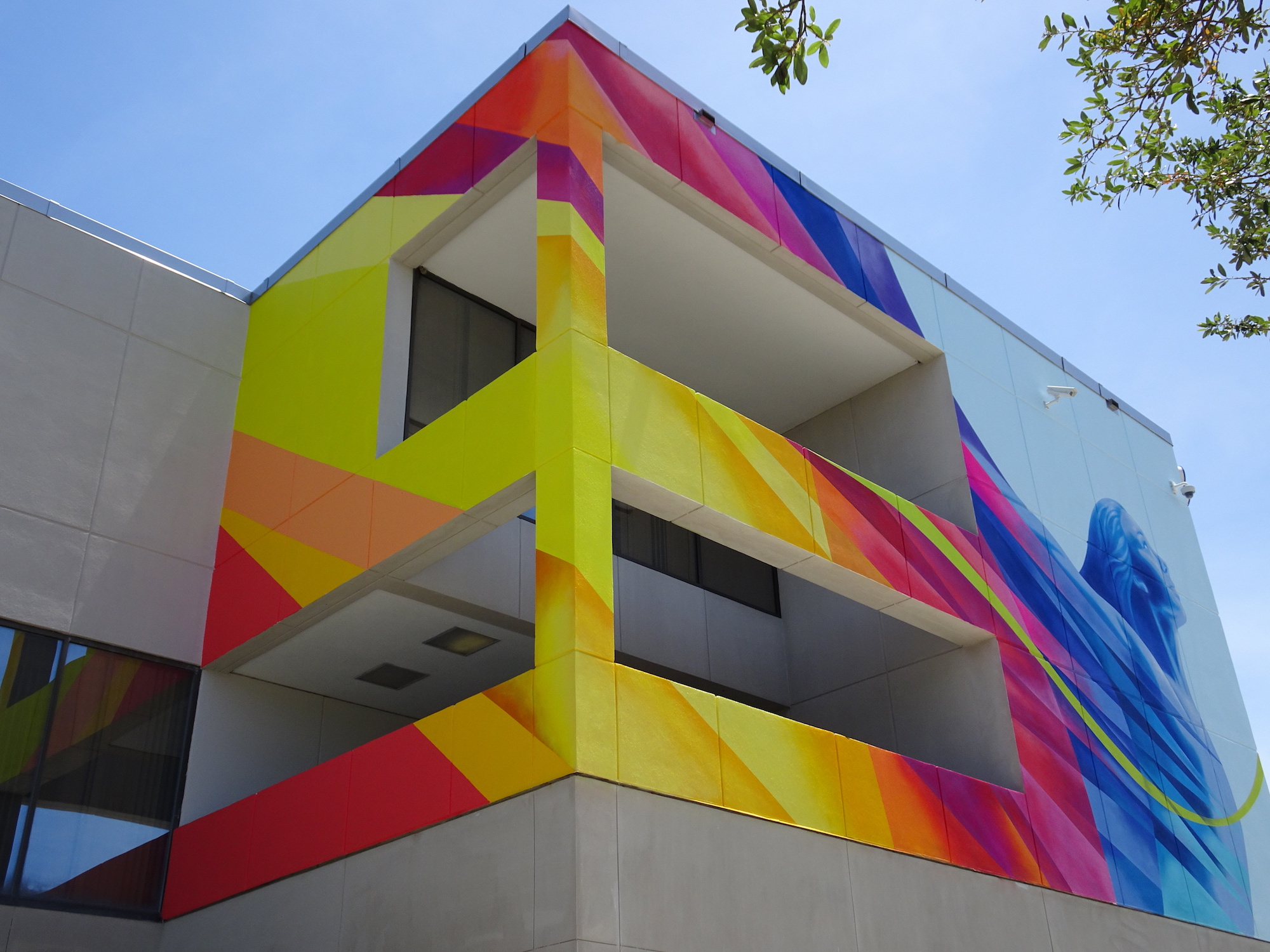 Outside colorful mural of woman with arms extending back like wings