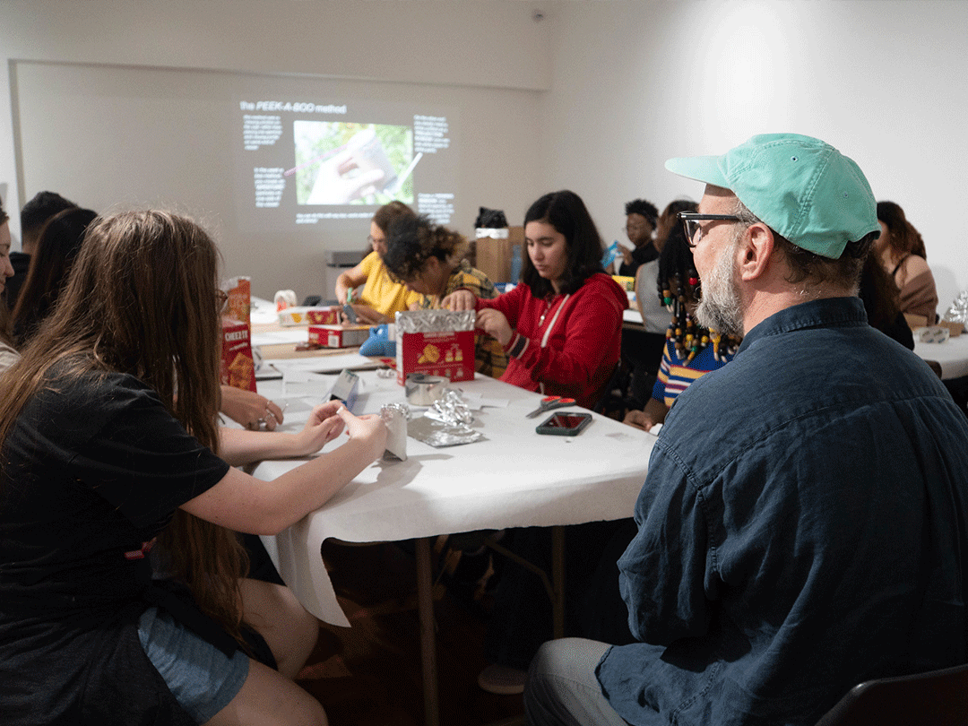  Several people seated at a table, focused on a projector screen displaying a presentation.