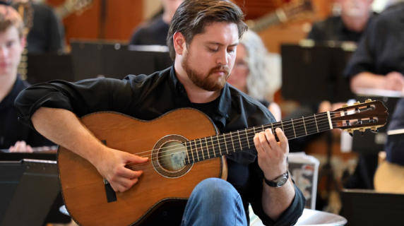 Photo of Kenneth Bender seated playing guitar