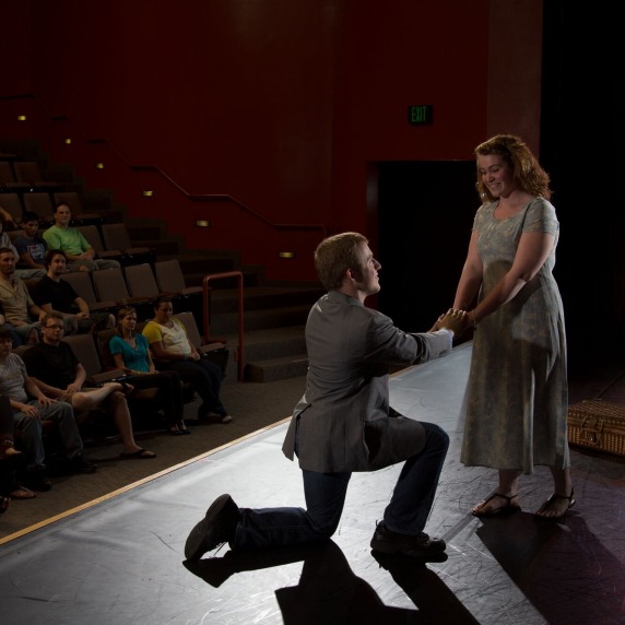 Actor on knees holding hands with actress