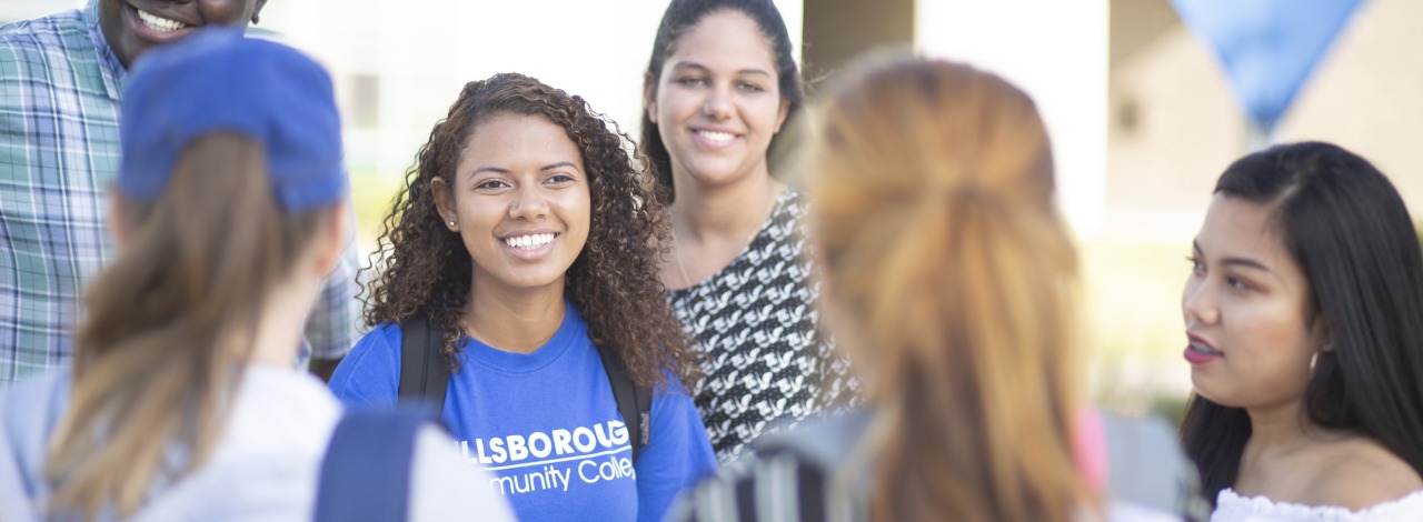 Group of diverse students hanging out outside, the center one is wearing a blue HCC t-shirt