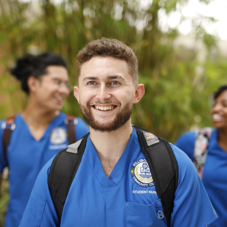 A nursing student smiling, with two other student walking behind him.